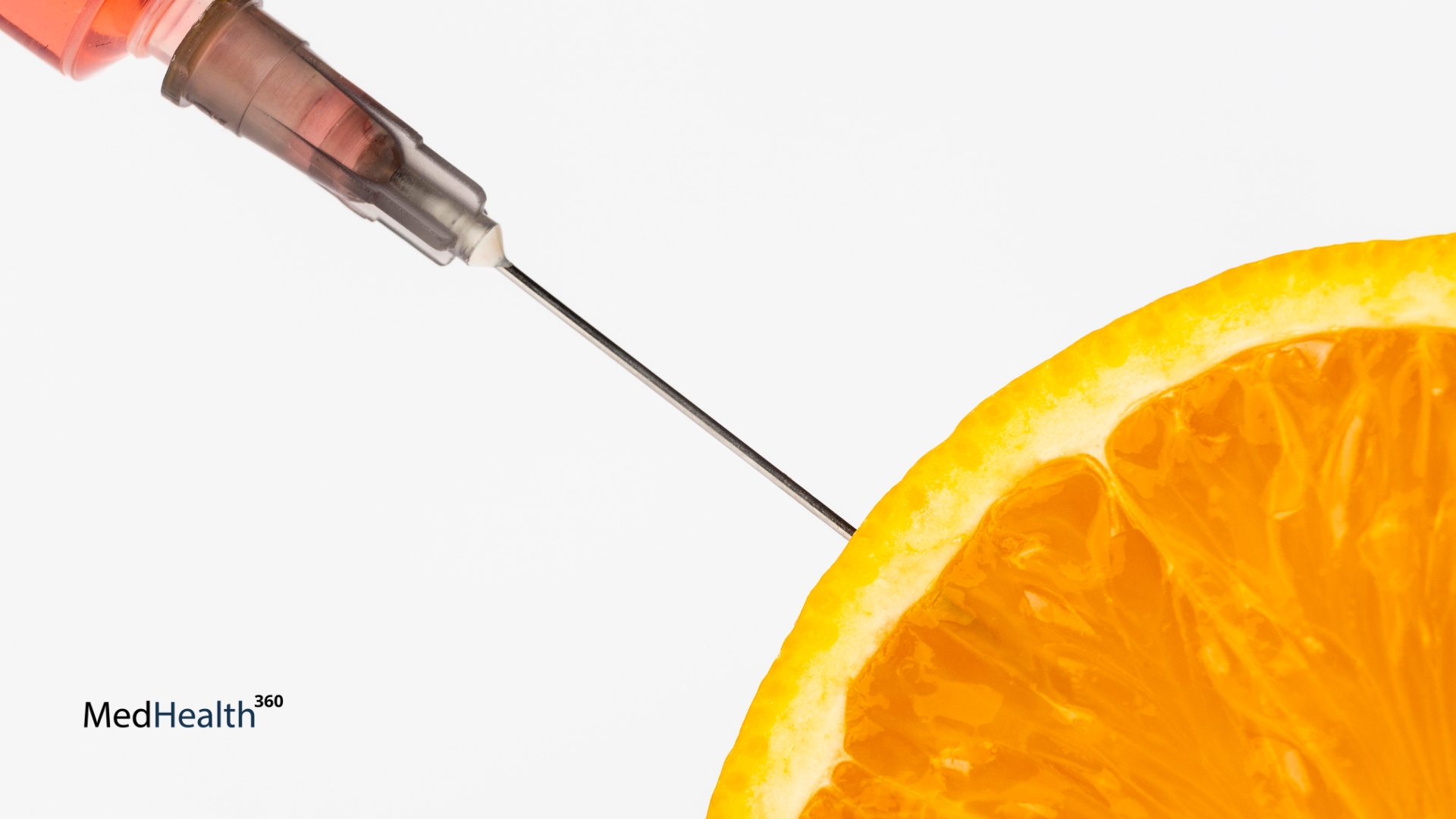 A syringe filled with orange liquid aimed at a fresh orange slice, symbolizing a vitamin C injection at MedHealth360.